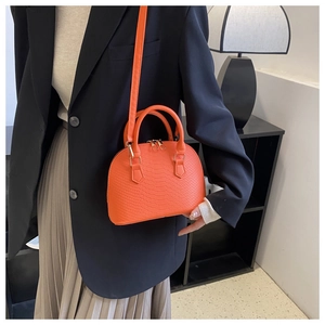 Detailed view of orange crocodile texture shell bag with gold hardware and shoulder strap