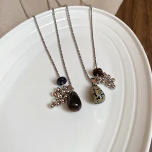Tiger eye and spotted stone tassel necklaces in a ceramic bowl on wooden background