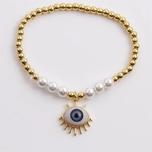 Detail of beaded evil eye bracelet with golden metal beads and white pearls on plain background