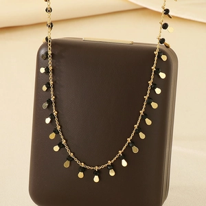 Detail of golden chain necklace with black beads and teardrop gold pendant charm