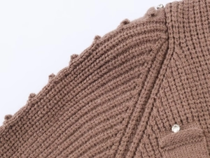Detail of brown chunky knit cardigan featuring scalloped edges and rhinestone accents