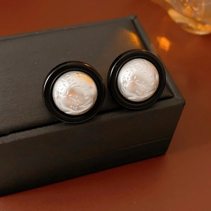 Close-up of round earrings with black outer rim and textured silver center on a box