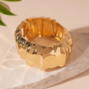 Close-up of golden wide cuff bracelet with wavy texture on a minimalist stone surface