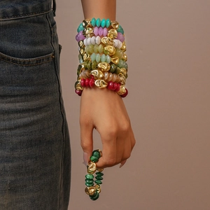 Close-up of stacked colorful acrylic beaded bracelets with irregular gold metal charms