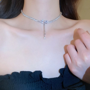 Close-up of silver bow necklace with sparkling zircon heart and delicate pearl tassel
