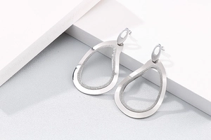 Détail de boucles d'oreilles gouttes argentées ajourées avec texture mate sur support blanc