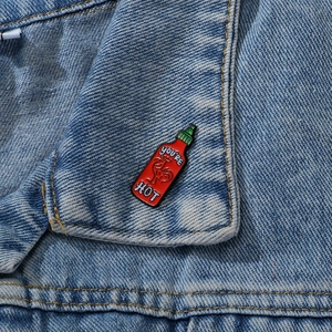 Cartoon red chili sauce enamel pin with You're Hot text on a blue denim jacket