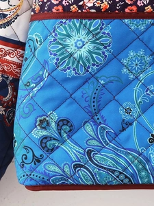 Detail of blue quilted fabric with paisley floral patterns and dark red piping trim