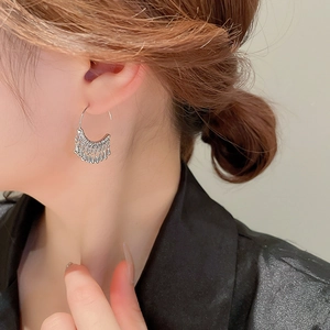 Detail of silver C-shaped metal tassel earrings with water drop charms on model