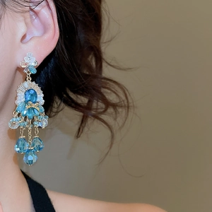 Dettaglio di orecchini di lusso a fiore con cristalli blu e perle indossati