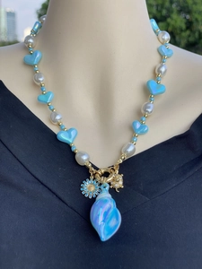 Dettaglio collana placcata oro 18k con ciondoli conchiglia e leone su perle blu