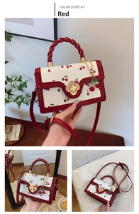 Detail of red cherry print handbag with golden flower clasp and twisted handle