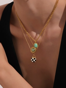 Detail of layered gold-plated necklaces with green stones and checkerboard bag pendant