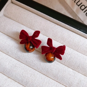 Detail of red velvet bow earrings with amber-toned resin beads on a cream fabric base