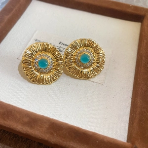 Macro shot of gold floral earrings with a blue gemstone and white zircon petals
