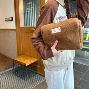 Detail of soft brown teddy fleece makeup bag with white label held by a model