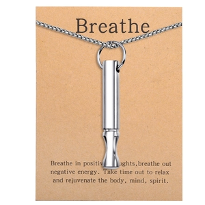 Close-up of silver cylinder breathing whistle pendant on a brown Breathe card