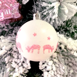 Close-up of white Christmas ball with pink glitter reindeer hanging on snowy tree