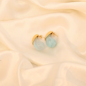 Detail of drop-shaped gold earrings with light teal marble resin on white silk