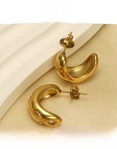 Détail de boucles d'oreilles C en acier titane doré avec zircone sur socle blanc