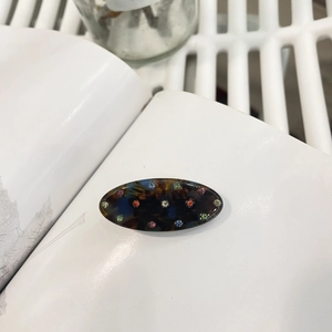 Oval tortoise shell hair clip with vibrant colorful rhinestones on a white background