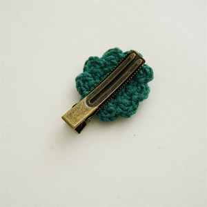 Vue détaillée du dos d'une fleur au crochet vert foncé avec une pince en métal bronze