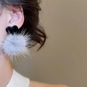 Dettaglio degli orecchini a cuore in tessuto con pompon grigio indossati da modella