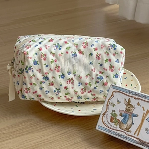 Detail of floral corduroy makeup bag with quilted texture and brand label on a plate