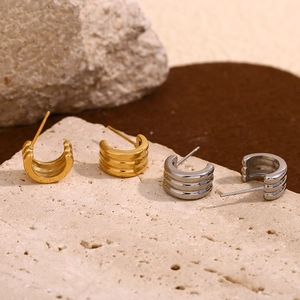 Macro detail of gold and silver triple-layered striped C-shape earrings on stone