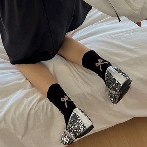 Detail of black ankle socks with pink bow patterns worn with sparkling silver shoes