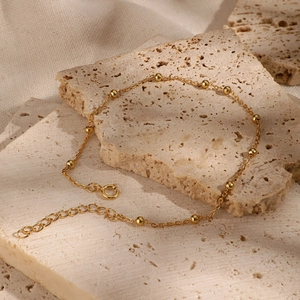 Detailed shot of golden bead chain bracelet on a stone tray with lobster clasp detail