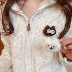 Detail view of cute plush cartoon brooches in brown and white on a knitted cardigan