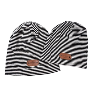 Detail of knitted beanie showing black and white stripes and brown leather brand patch