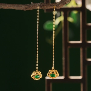 Detail of vintage gold cloud earrings with green jade pendant on a wooden branch