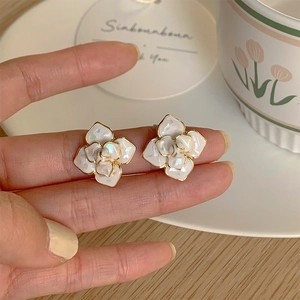 Close-up of white camellia earrings with iridescent petals and gold-lined layered detail