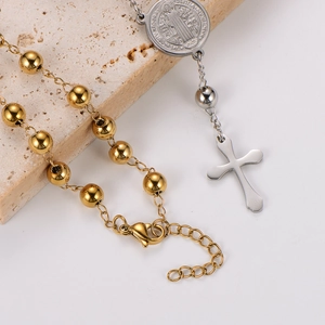 Macro detail of gold bead chain with Saint Benedict medal and silver mirror cross pendant