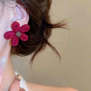 Detailed close-up of a red flocked flower earring with a soft velvet texture on a model