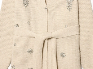 Détail d'un cardigan beige avec motifs floraux en cristal et ceinture à nouer assortie