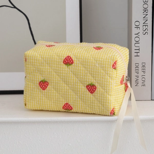 Close-up of quilted cotton makeup bag with strawberry print and white ribbon zipper pull