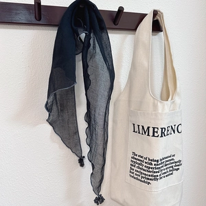 Detail of a navy blue sheer scarf with tassels hanging on a hook next to a canvas tote bag