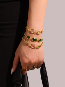 Stacked colorful oval gemstone bracelets and gold rings shown on model wrist with handbag