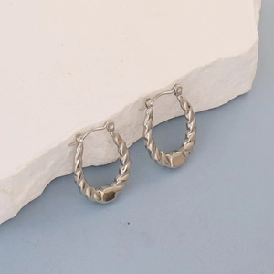 Macro detail of twisted silver stainless steel hoop earrings on white stone background
