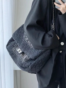Detail of black quilted denim shoulder bag with silver chain strap and metal clasp