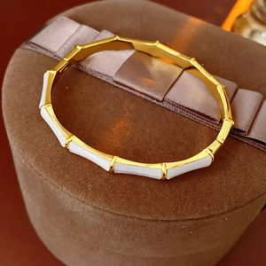 Detailed view of a gold bamboo-style bracelet with white mother-of-pearl insets on a velvet box