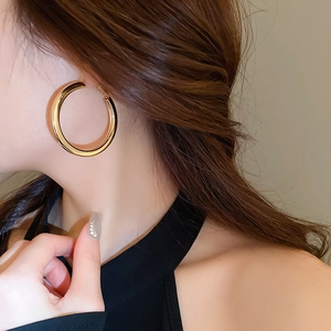 Close-up of chunky gold hoop earring worn by a model showcasing polished metal texture