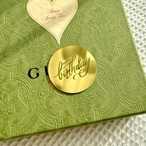 Macro shot of circular golden mirror acrylic Happy Birthday cake topper on green gift box