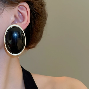 Gros plan d'un modèle portant des boucles d'oreilles ovales en résine noire et bordure dorée