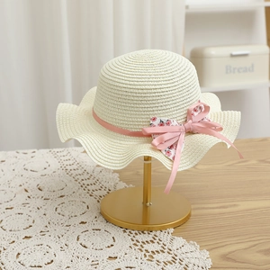 Détail d'un chapeau de paille crème avec bord ondulé et nœud fleuri rose doux