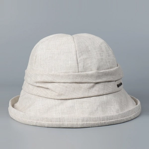 Detail shot of linen bucket hat texture with decorative pleats and metal logo plate