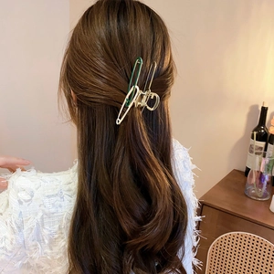 Detail of a golden safety-pin style hair claw with forest green accents on wavy hair